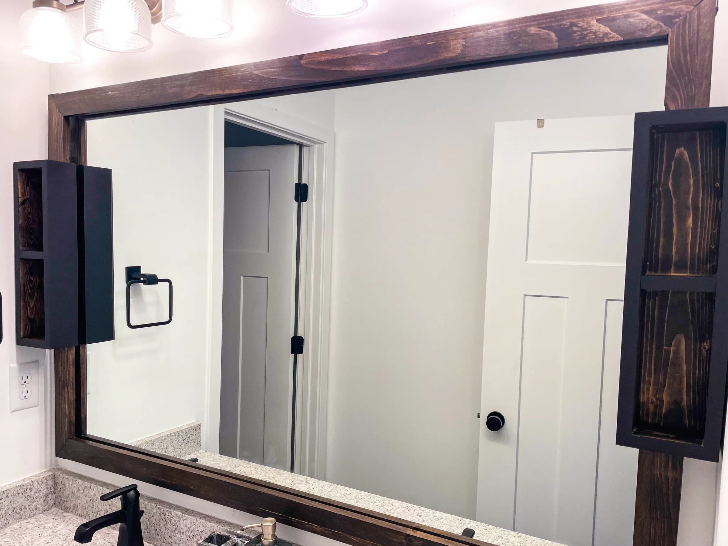Custom dark wood mirror frame and wall cabinets in a bathroom