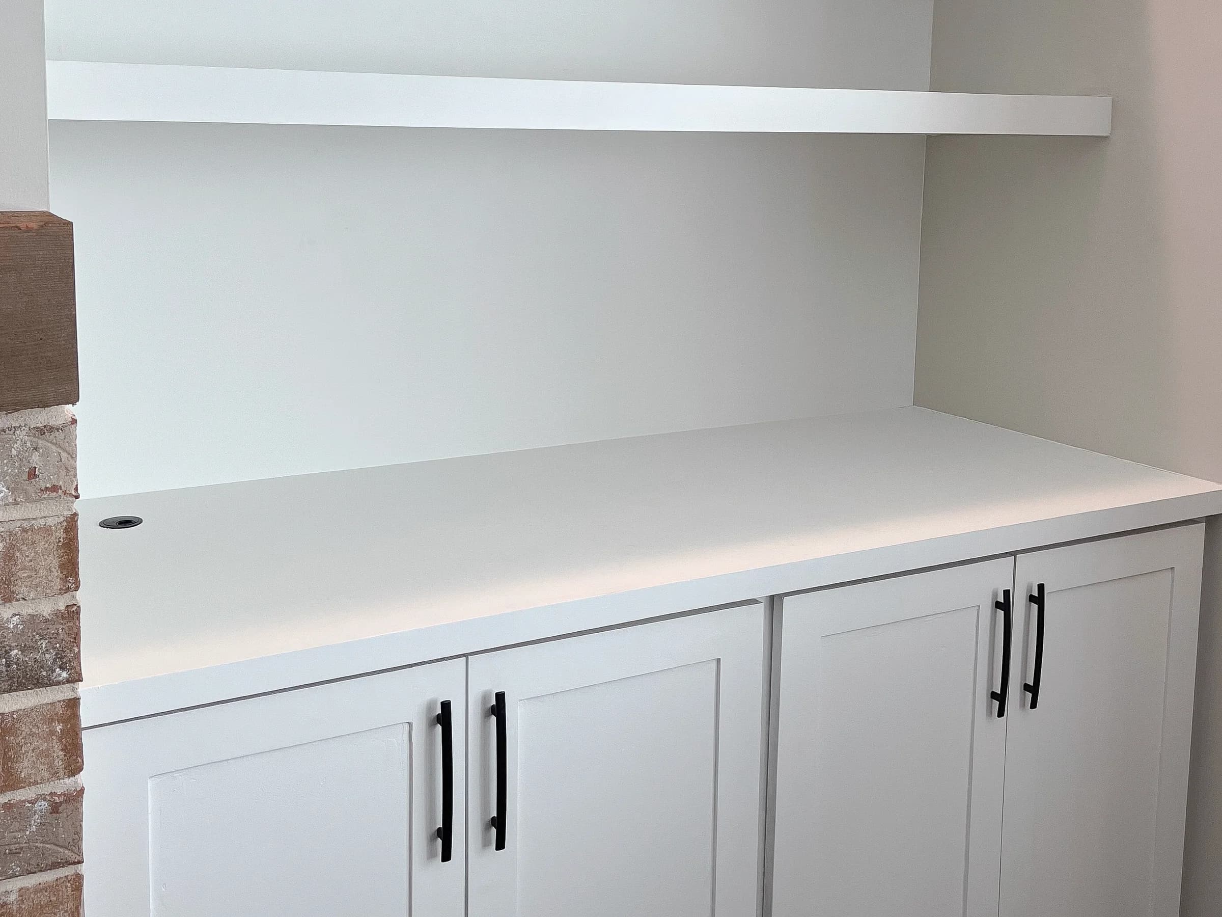 White built-in cabinets with a counter and open shelf beside a brick fireplace