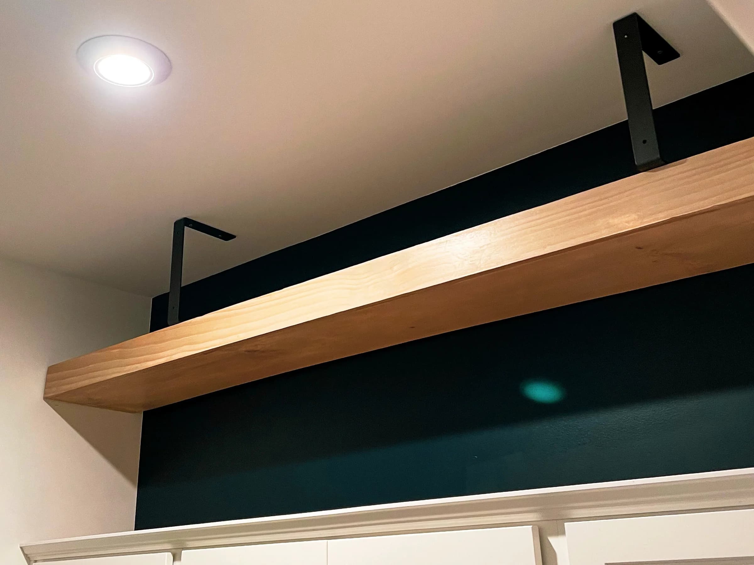 Thick wood shelf mounted on black metal brackets above a doorway