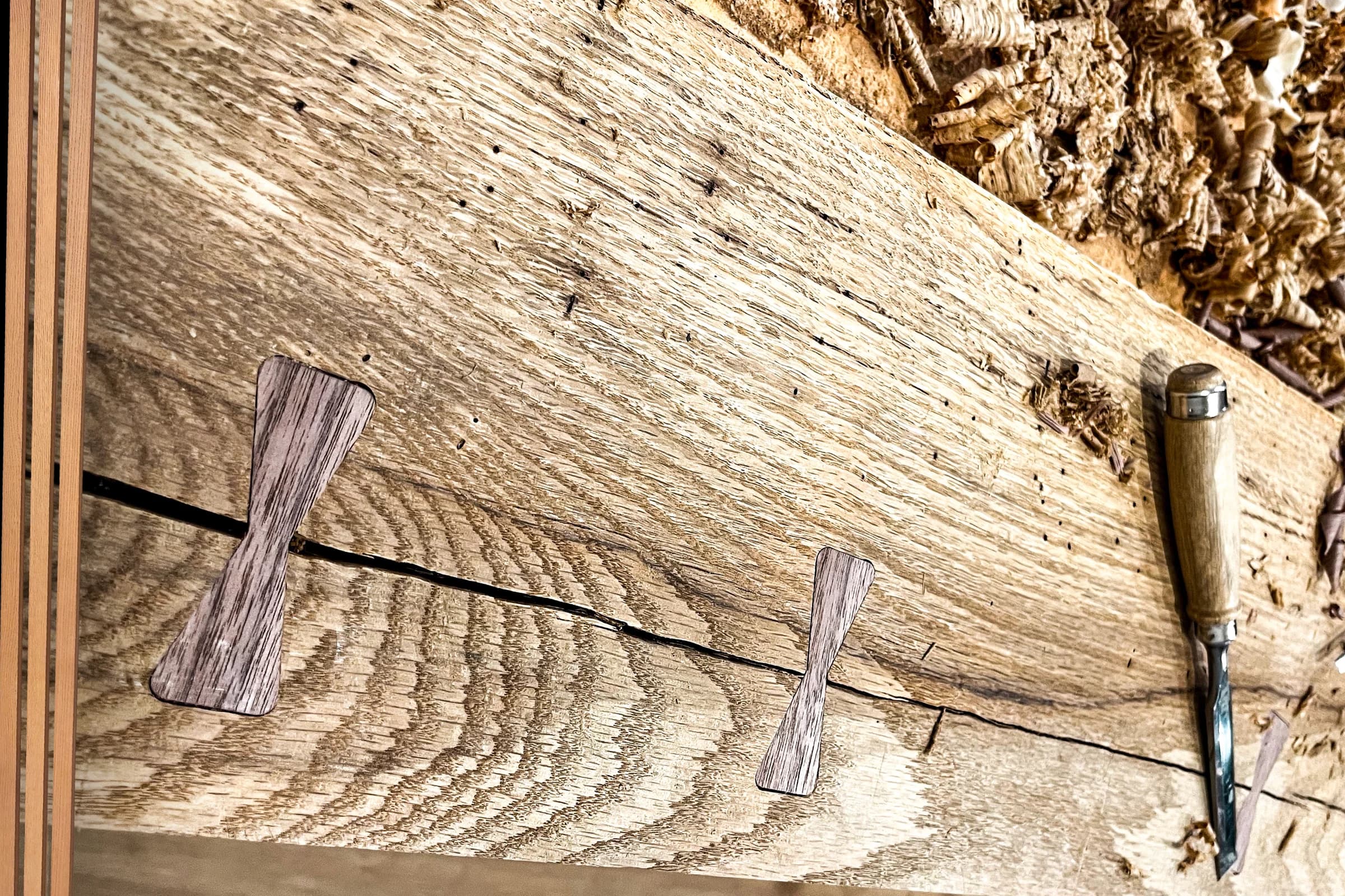 Close-up of a live edge wood tabletop with butterfly joints and a chisel