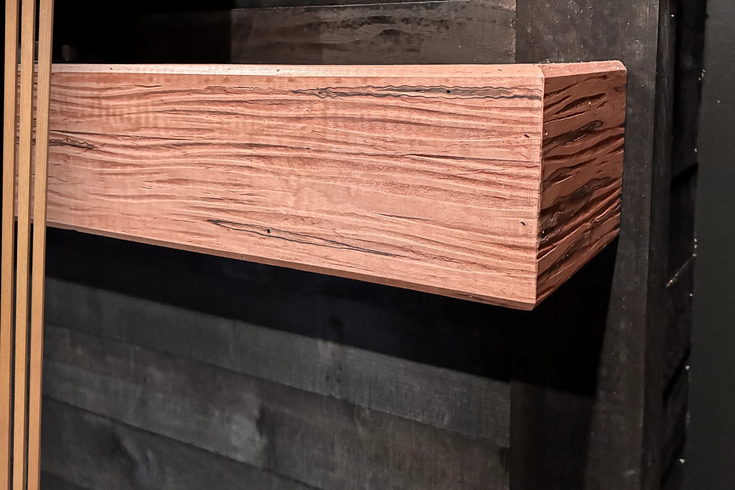 Solid wood fireplace mantel with prominent grain against a dark surround